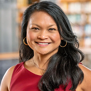 Headshot of a smiling woman with dark wavy hair, gold hoop earrings, and a red top.