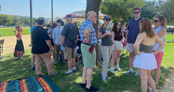 A group of people talking and hanging out on the grass during an outdoor community picnic.