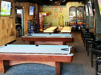 A game lounge with pool tables, shuffleboard, arcade machines, TVs, and a "Beer Garden" sign pointing down a hall.