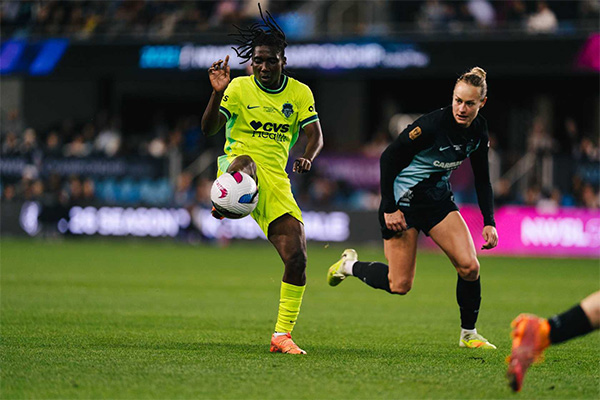 A soccer player in a yellow jersey controls the ball with her knee as a defender in black closes in.