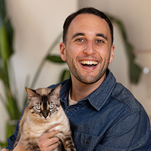 Headshot of Cory Epstein, a smiling man with a light beard holding a Bengal cat.
