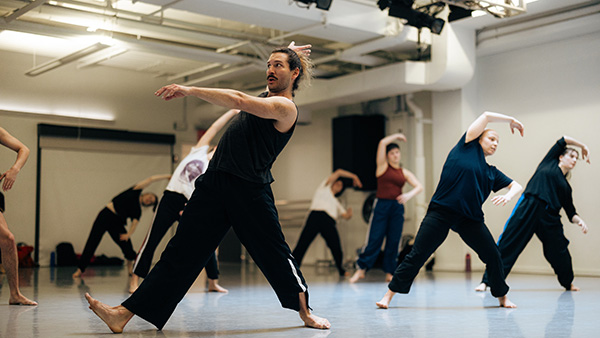 A group of contemporary dancers in casual practice wear rehearse choreography in a bright studio.