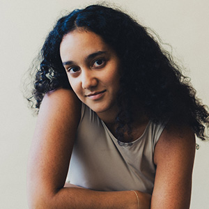Headshot of Soraya, a woman with dark, curly hair resting her arms on a surface.