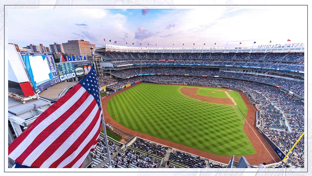An American flag waving over a high-angle view of a crowded Yankee Stadium during a game.